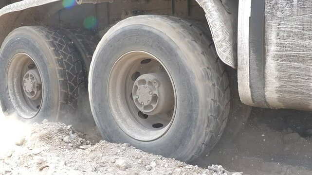 The wheels of a large heavy truck stuck in sandy soil. The heavy truck tries with great effort to get onto flat, hard ground.