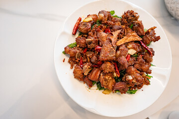 fried sticky ribs marinated in soy sauce and ginger sprinkled on white dish on marble table, chineese style, view from above