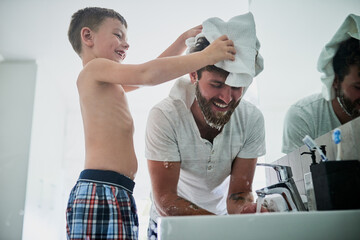Playful, child and man with towel in bathroom for hygiene, bonding and getting ready together. Happy, father and son laughing with cloth by water for washing hair, teaching and morning routine
