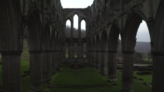 Drone shot exploring the historical Rievaulx Abbey ruins surrounded by lush green landscape in North Yorkshire, England