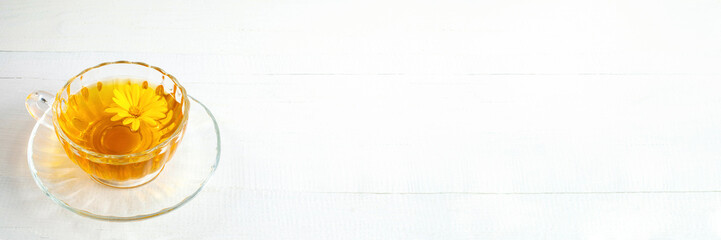 Banner. Glass cup with calendula tea and fresh flower in it on white wooden table. Herbal medicine.