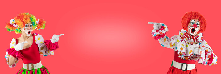 Funny clowns pointing at blank template copy spase for advertising, posters, greetings, invitations. Entertainer as Joker in a suit and wig, with clown whiteface makeup