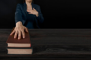 Female hand on the Bible and on the constitution book during the inauguration in parliament or the oath in court. Woman taking Oath of Office. Dark background, blue office clothes.