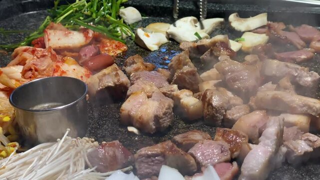 Korean Pork belly is being cooked on a grill. The meat is brown and has a lot of smoke coming off of it