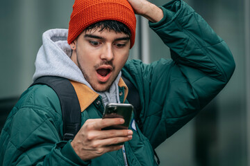 young man with mobile phone on the street with surprised expression