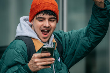 young man with mobile phone on the street excited celebrating
