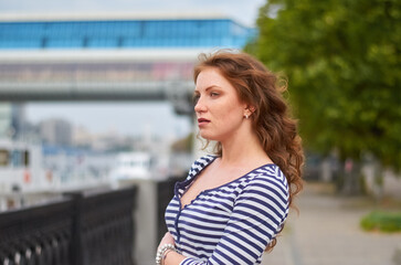 Obraz premium A woman in a striped shirt and white skirt stands on a pier against the backdrop of tall buildings.