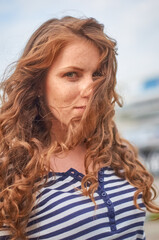 A woman in a striped shirt and white skirt stands on a pier against the backdrop of tall buildings.