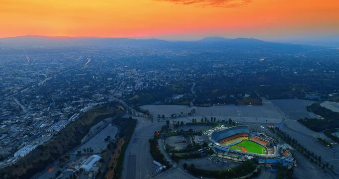 Dodger Stadium in Los Angeles, California, USA. Densely populated cityscape around the stadium. Orange sky above the mountain range at backdrop. Top view.