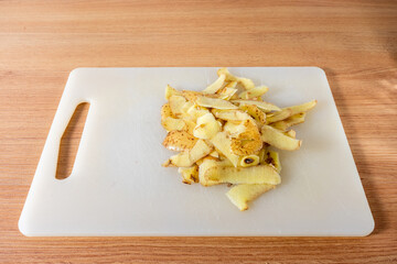 Freshly peeled potato skins scattered on a non-wooden cutting board, showcasing the rustic beauty of kitchen prep work.