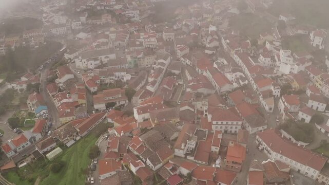 Drone shot of the picturesque Monchique town with mist covering the rooftops of traditional houses in Portugal.