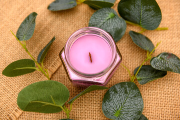 Pink scented candle on wooden table with eucalyptus leaves. Top view on canvas.