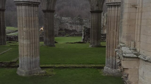 Drone footage of ancient Rievaulx Abbey ruins, capturing the medieval architecture and natural surroundings in North Yorkshire, England.