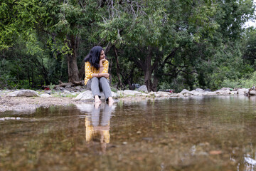 Isolated Girl Sitting Alone on Stone at Calm Lake Shore in the Morning