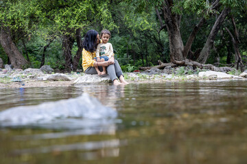 Fototapeta premium Isolated Woman Spending Quality Time with Son on Stone at Calm Lake Shore in the Morning