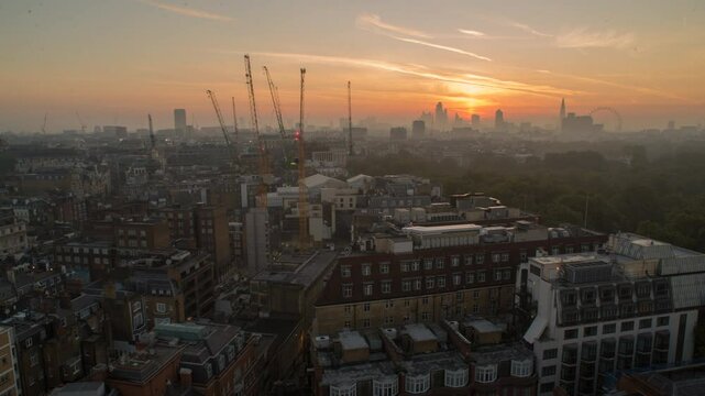 Timelapse of sunrise over London's skyline, with construction cranes and buildings in the foreground and the city waking up in the distance, London, UK