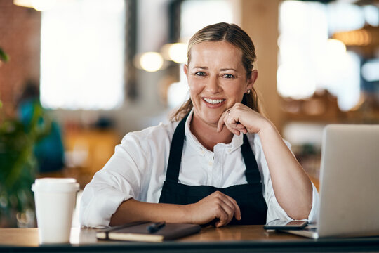 Woman, face and laptop in cafe for planning, catering service and recipe development with apron. Entrepreneur, portrait and smile in bakery for small business, online menu and management with startup