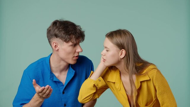 Positive couple of young boyfriend and girlfriend in yellow blue clothes isolated on green background man and woman listening eavesdropping and talking.