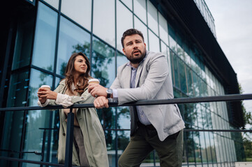 Business people enjoying coffee break leaning on railing in front of office building