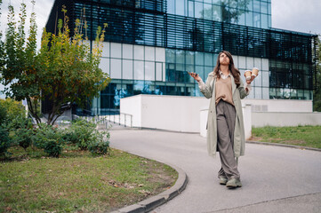 Businesswoman walking with coffee and phone looking up