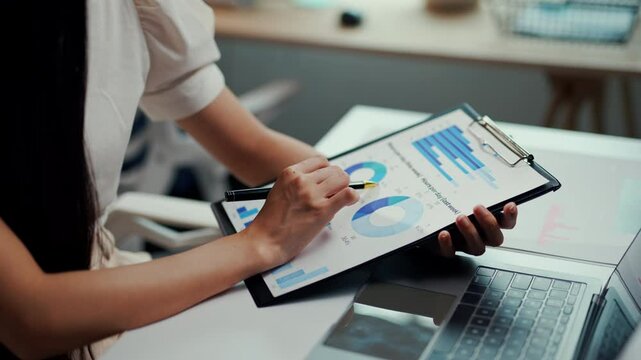 Businesswoman analyzing financial data on a chart while seated at her desk, focusing on insights and trends for decision making