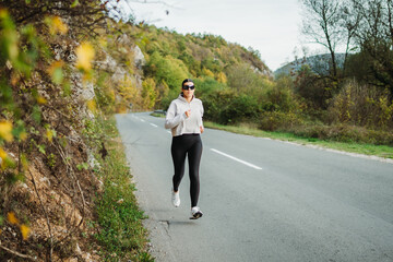 Fototapeta premium Young caucasian woman running or jogging on the country road 