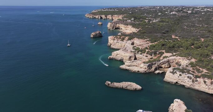 Aerial drone view from drone flying over Benagil sea caves and Atlantic Ocean coastline in Benagil, Algarve, Portugal, Europe. Boats sightseeing in the Mediterranean. Shot in 5K ProRes 422 HQ