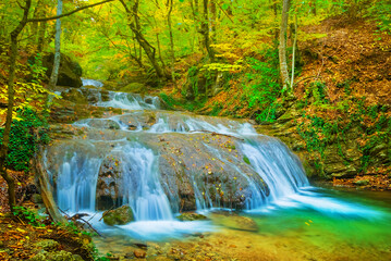 waterfall on small mountain river rushing through canyon covered by red dry leaves
