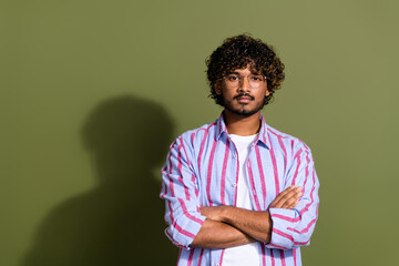 Obraz premium Photo of serious confident guy with wavy hair dressed striped shirt in glasses holding arms crossed isolated on khaki color background