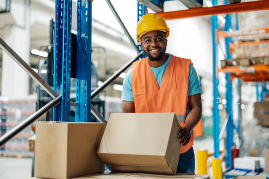 Warehouse worker holding cardboard box smiling at camera