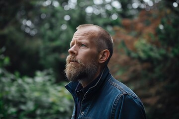 Naklejka premium Forester with a beard is standing in a forest and looking up with a thoughtful expression
