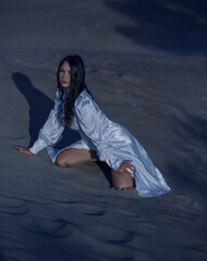 Glamorous brunette girl poses on the sand at night in a sexy dress showing her legs.