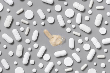 White medical capsules and pills with opened beige capsule in the middle on grey top view