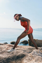Woman stretching on rocky shore by the sea in a vibrant red outfit