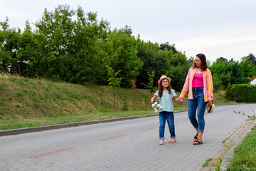 Young woman and her little girl are walking along the road. Mother and daughter are walking together.