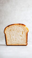 Freshly baked slice of bread is standing upright, showcasing its soft texture and golden-brown crust. The neutral background emphasizes the simplicity and inviting nature of the bread