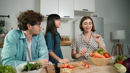 Happy father move to music while cooking food and prepare lunch at modern kitchen. Active dad dancing to song while making healthy food or salad surrounded with vegetable and kitchenware. Pedagogy.