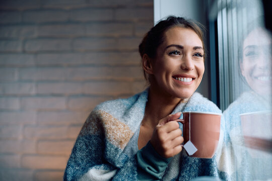 Happy woman enjoying cup of warm tea by  window.