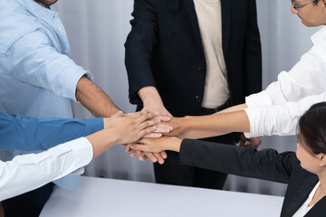 Fototapeta premium Group of diverse office worker join hand together in office room symbolize business synergy and strong productive teamwork in workplace. Cooperation and unity between business employee. Prudent