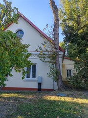 An old building with striking red brick pillars and a pitched roof, surrounded by greenery. This...
