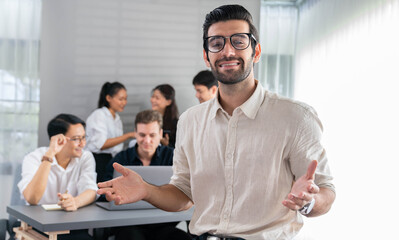 Confidence and happy smiling businessman portrait with background of his colleague and business team working in office. Office worker teamwork and positive workplace concept. Prudent