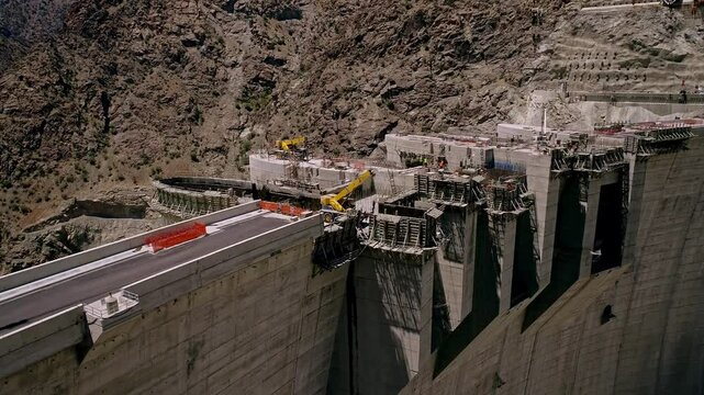 The video shows the ongoing construction of a large dam, featuring significant progress in the structure, with workers and large machinery actively operating on site.