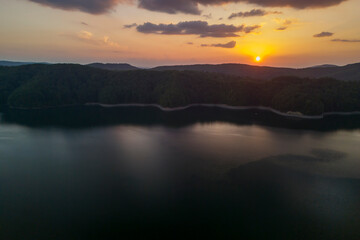 A stunning sunset over a tranquil lake surrounded by lush forests. The calm water reflects vibrant colors, creating a serene and picturesque landscape perfect for nature lovers.
