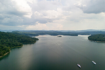 Aerial view of a calm lake surrounded by lush green forests under a cloudy sky. Tranquil nature scene ideal for relaxation and escape.