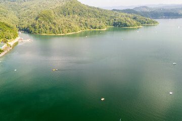 Fototapeta premium Aerial view of a serene lake surrounded by lush green hills under a clear sky, perfect for nature lovers and outdoor enthusiasts