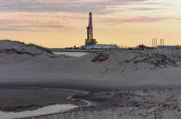 Drilling oil and gas wells in desert terrain. Sand hills, sparse vegetation. Beautiful sky. Infrastructure of the drilling rig