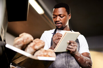 Black man, baker and writing with pastry for ingredients, new recipe or texture at factory. Young...