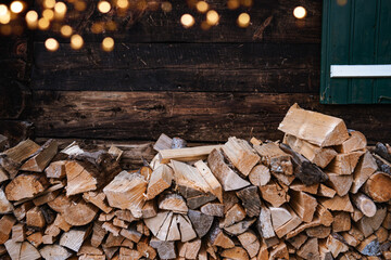 Stack of firewood along an outside wall of a hause with green shutters and golden bokeh. Horizontal...