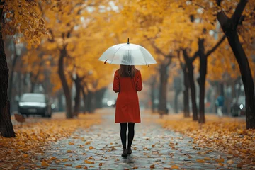 Selbstklebende Fototapeten A lonely thin girl in a red coat walks under an umbrella in an autumn park with her back to the viewer  © ashva