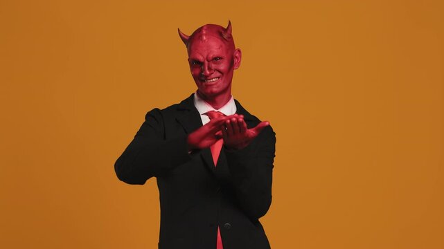 Devil businessman rubbing hands together on orange background